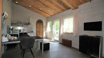 A spacious kitchen with modern appliances, a dining area with a table and chairs, a large window with curtains, and a flat-screen TV mounted on the wall.