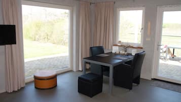 A modern room with a dining table, chairs, a television, and large windows with curtains.