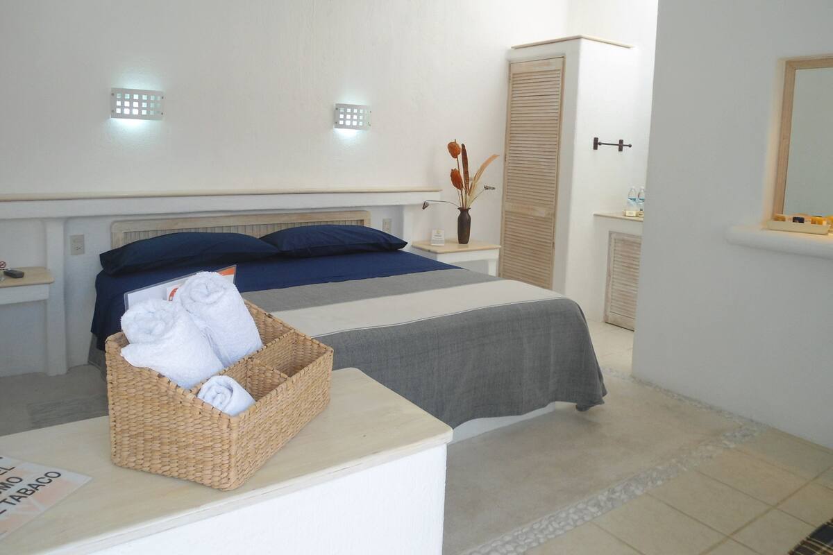 Ein Schlafzimmer mit einem Bett, einem Nachttisch, einer Wandlampe, einem Spiegel und einer kleinen Vase mit Blumen.