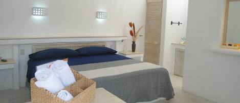 Quarto com cama, mesa de cabeceira, luminária na parede, espelho e pequeno vaso com flores.