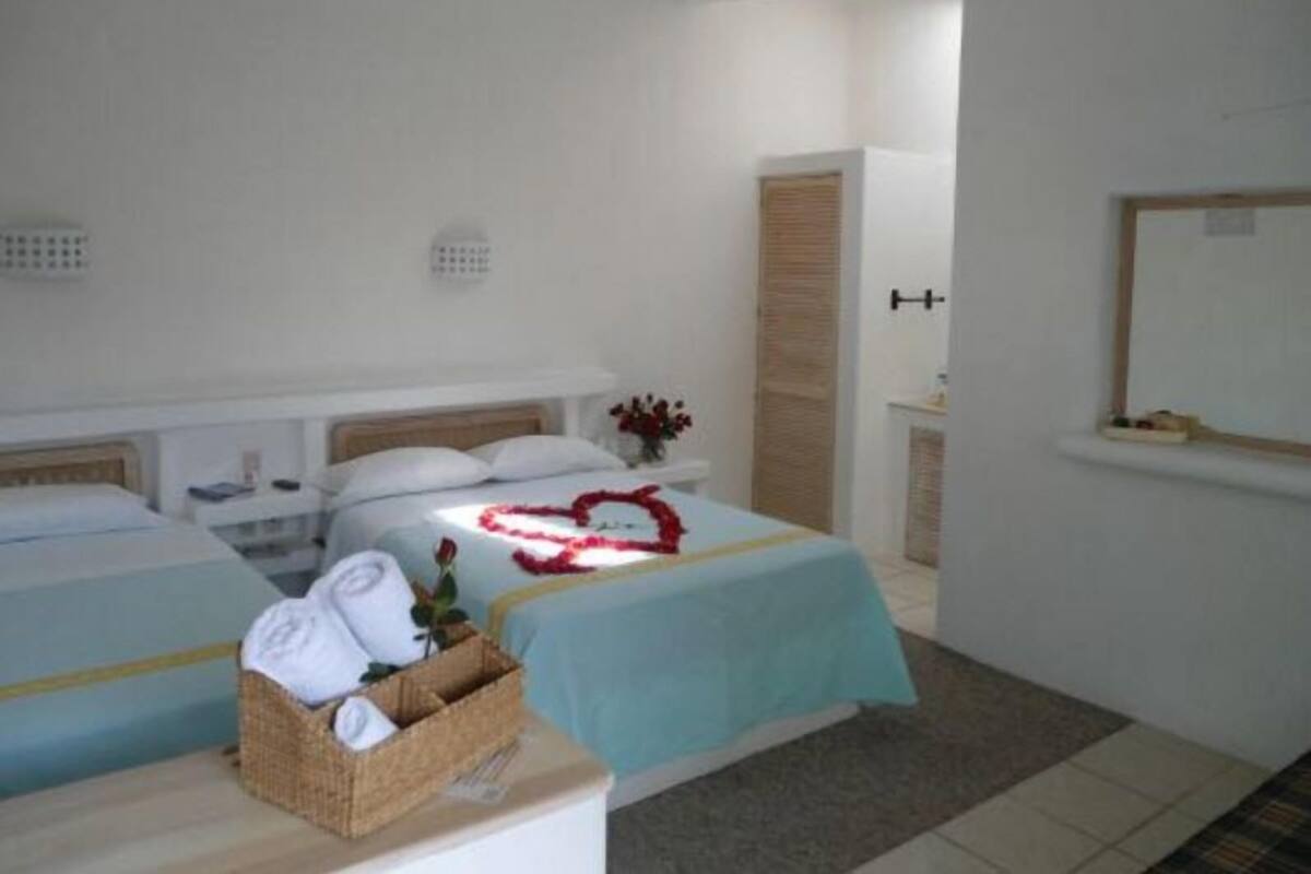 Ein Hotelzimmer mit zwei Betten, einem kleinen Tisch mit einem Wäschekorb voller Handtücher und einem Spiegel an der Wand.