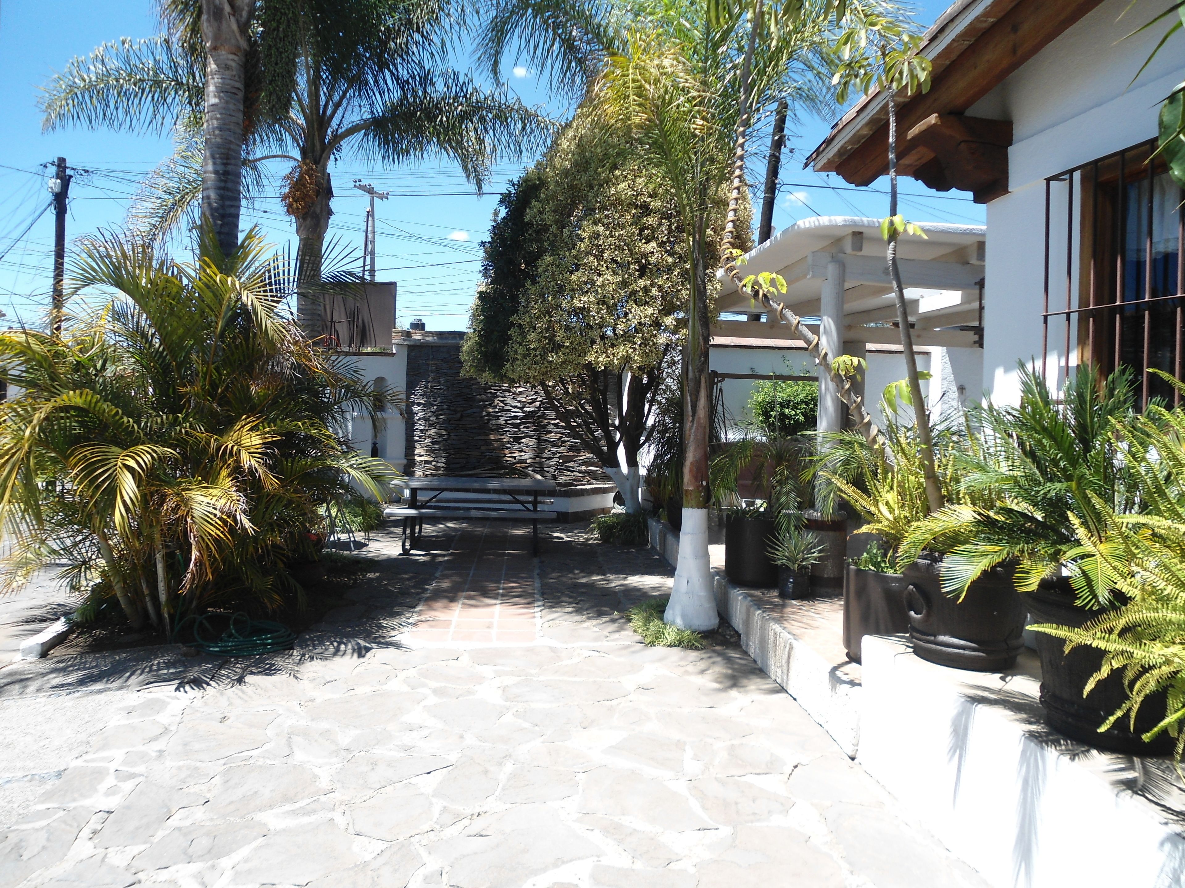 A paved pathway leading to a building with a stone wall and a wooden pergola.