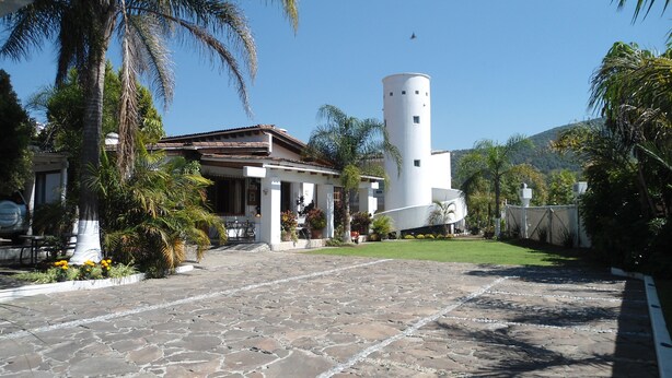 A courtyard with a stone floor, palm trees, and a white building with a cylindrical tower.