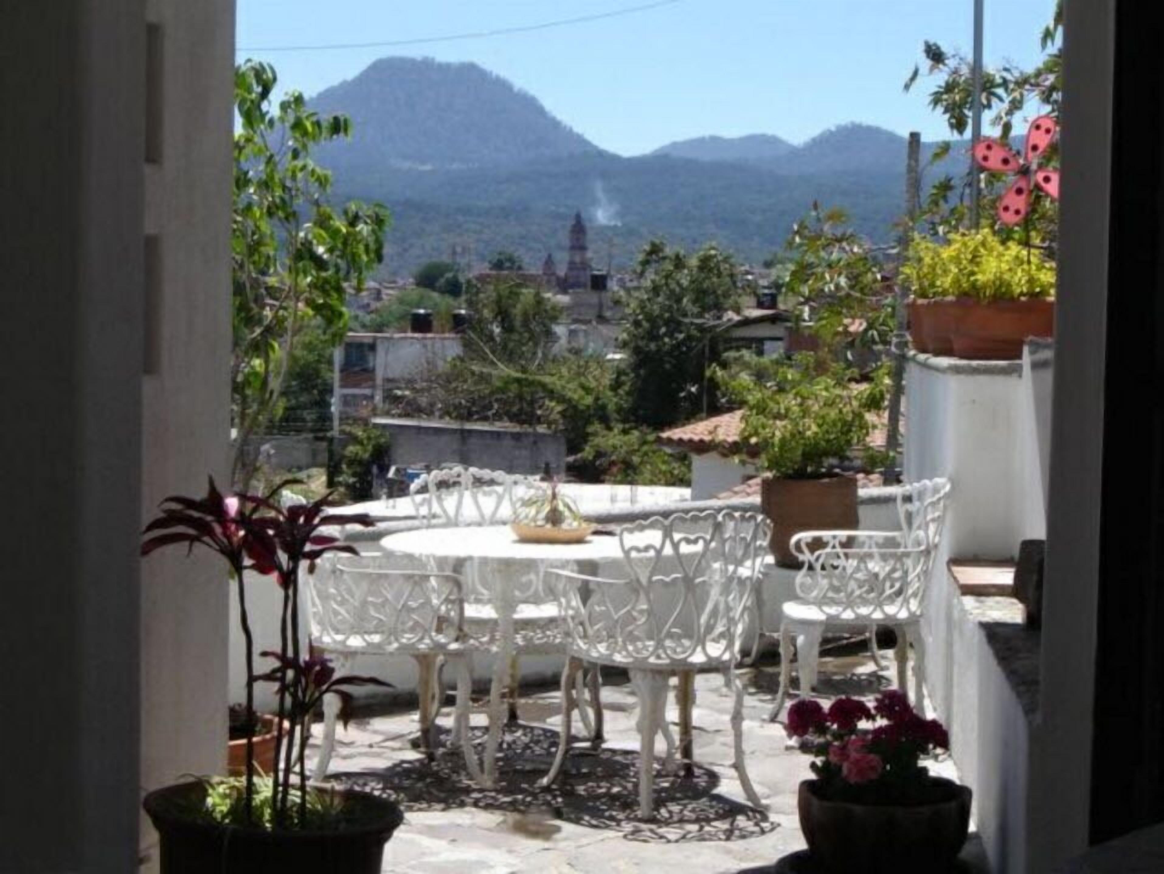A patio with white chairs and tables, surrounded by potted plants and a view of mountains.