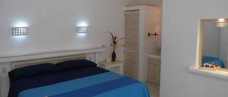 Un dormitorio con cama, mesitas de noche, un espejo y un buró.