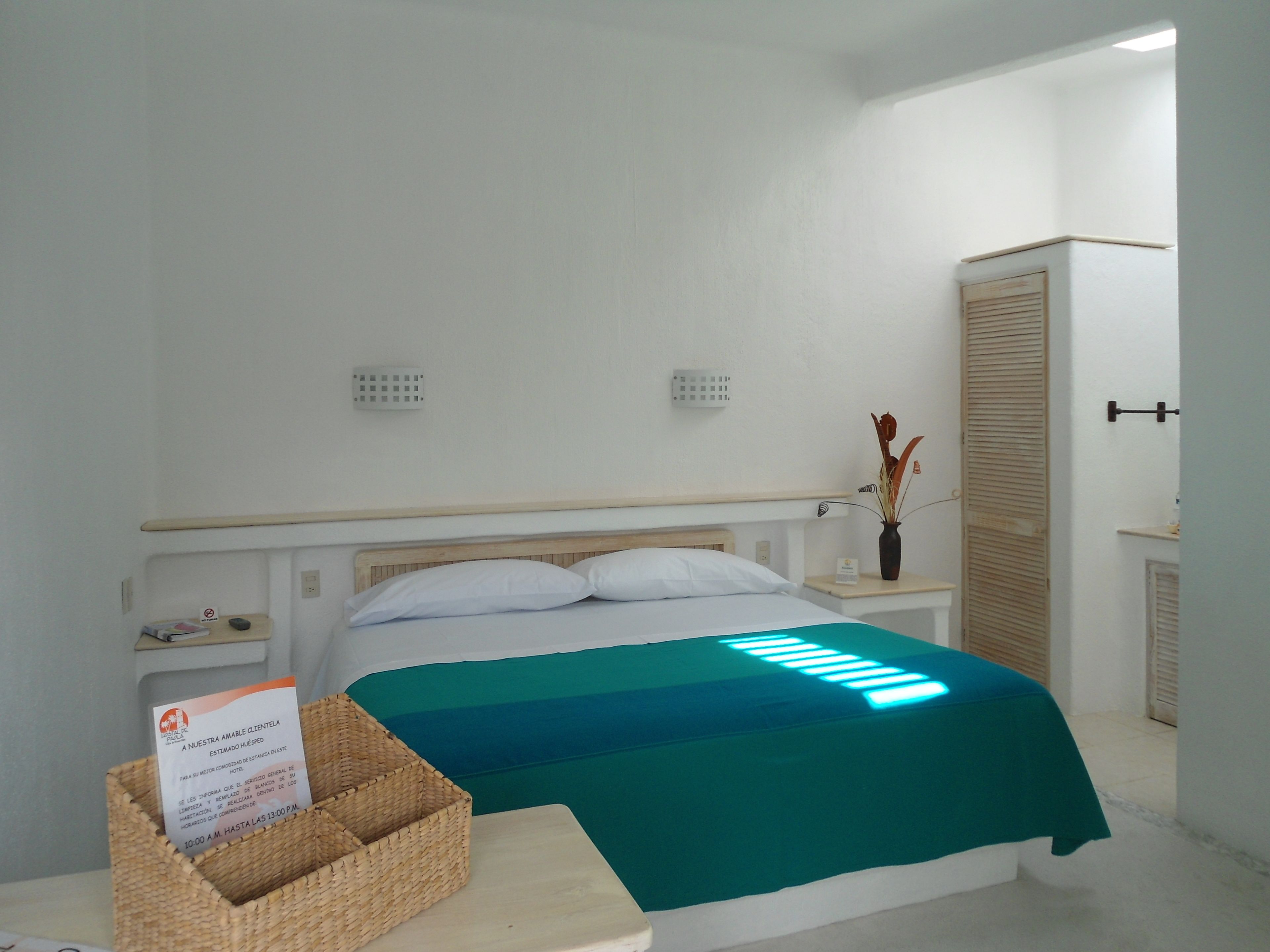 Une chambre d’hôtel avec un lit, une table de chevet, une petite table de nuit avec un vase, une armoire et un panneau sur la table de chevet.