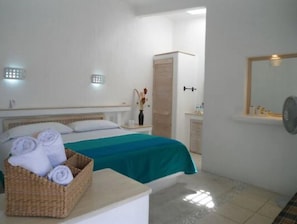 Ein Hotelzimmer mit einem Bett, einem Nachttisch mit einer Tablett voller Handtücher, einem Spiegel und einem kleinen Schrank.