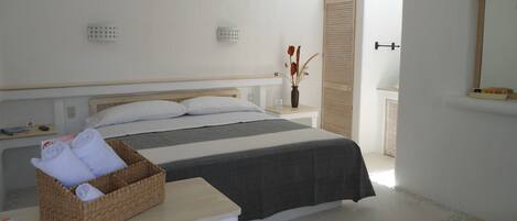 Un dormitorio con cama, una mesita de noche con una cesta de toallas, una mesita auxiliar, un aparador y un espejo en la pared.