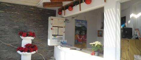 Un área de recepción con pared de piedra, mostrador blanco, tablón de anuncios y techo de madera.
