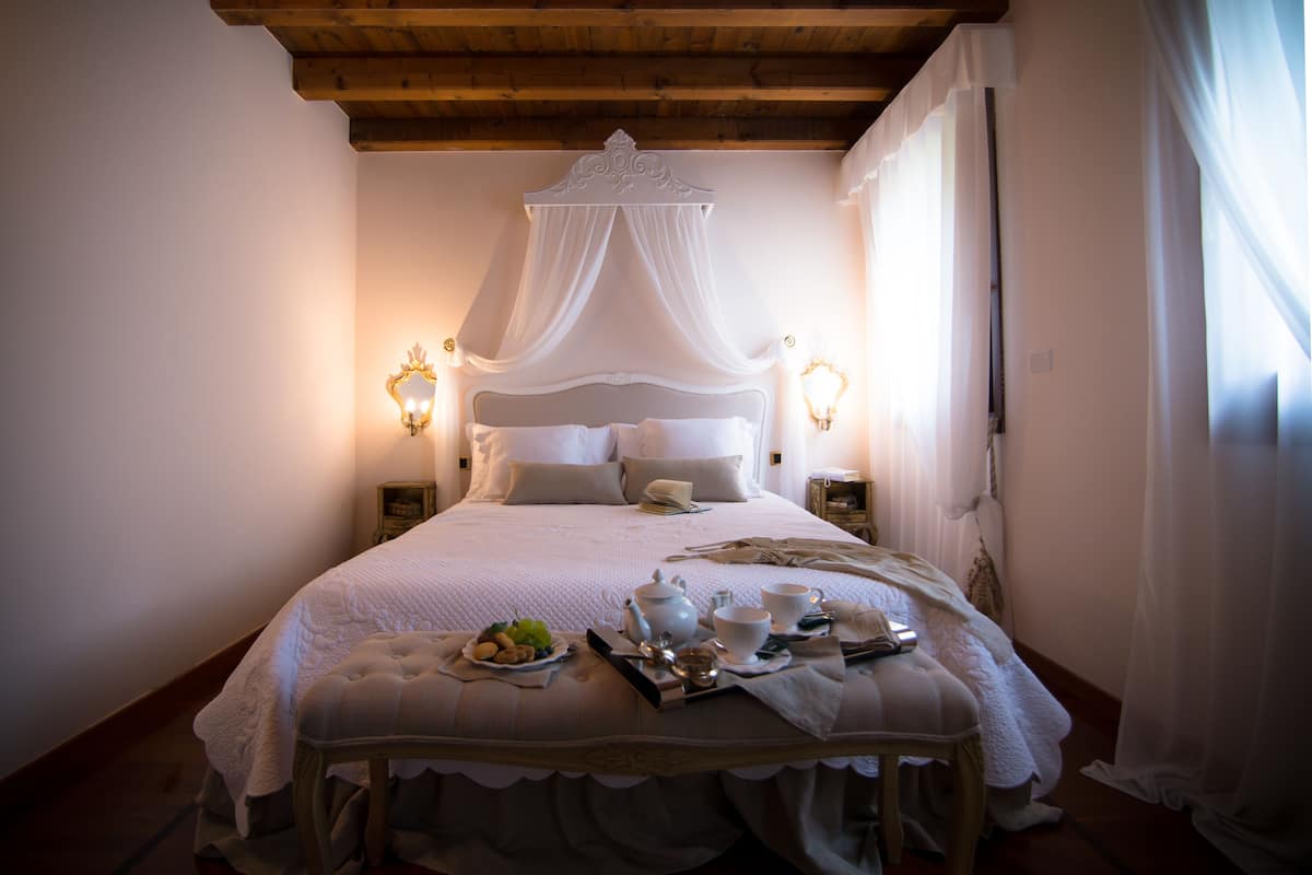 A neatly made bed with a canopy, bedside tables with lamps, and a tray of breakfast items on the bed.