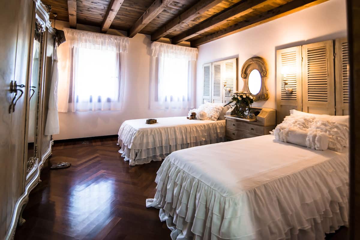 A bedroom with two beds, wooden flooring, a mirror, and a dresser.