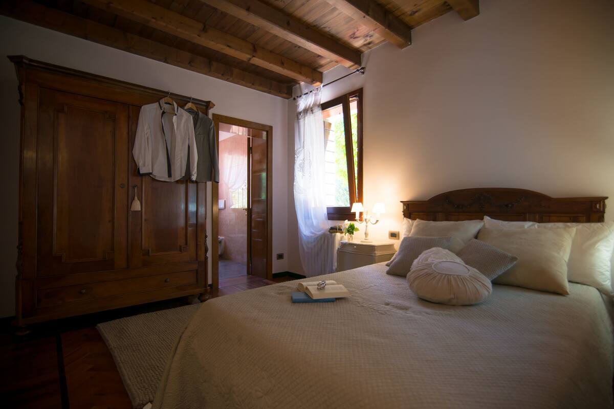 A bedroom with a wooden bed, a nightstand, a wardrobe, and a window with curtains.