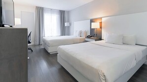 A hotel room with two beds, a desk with a chair, a TV, and a lamp. - Le Grand Hôtel (Baie Comeau)