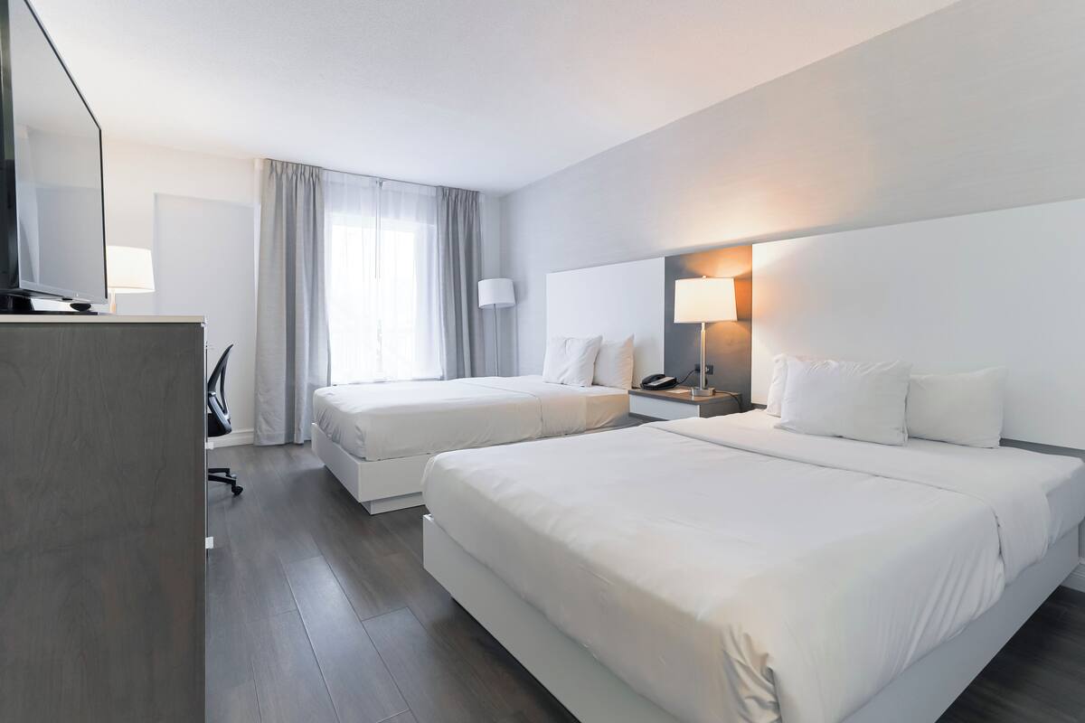 Une chambre d’hôtel avec deux lits, un bureau avec une chaise, une télévision et une lampe.