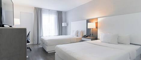Une chambre d’hôtel avec deux lits, un bureau avec une chaise, une télévision et une lampe.