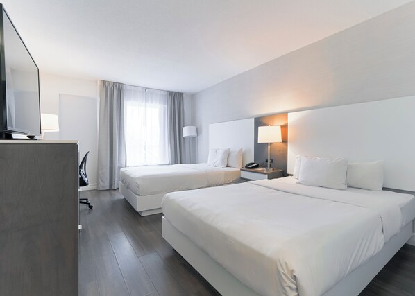 A hotel room with two beds, a desk with a chair, a TV, and a lamp. - Le Grand Hôtel (Baie Comeau)