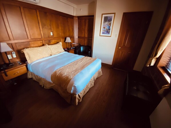 Una habitación de hotel con una cama grande, paneles de madera en las paredes, un escritorio con una lámpara y una silla.