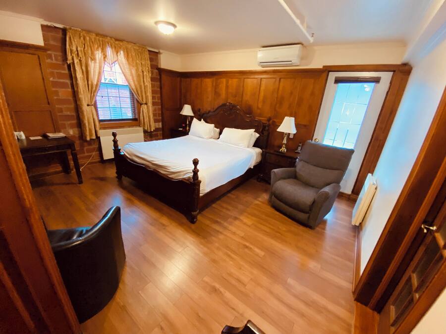 Un dormitorio con cama de madera, una silla, una mesita de noche, una ventana con cortinas y un equipo de aire acondicionado.
