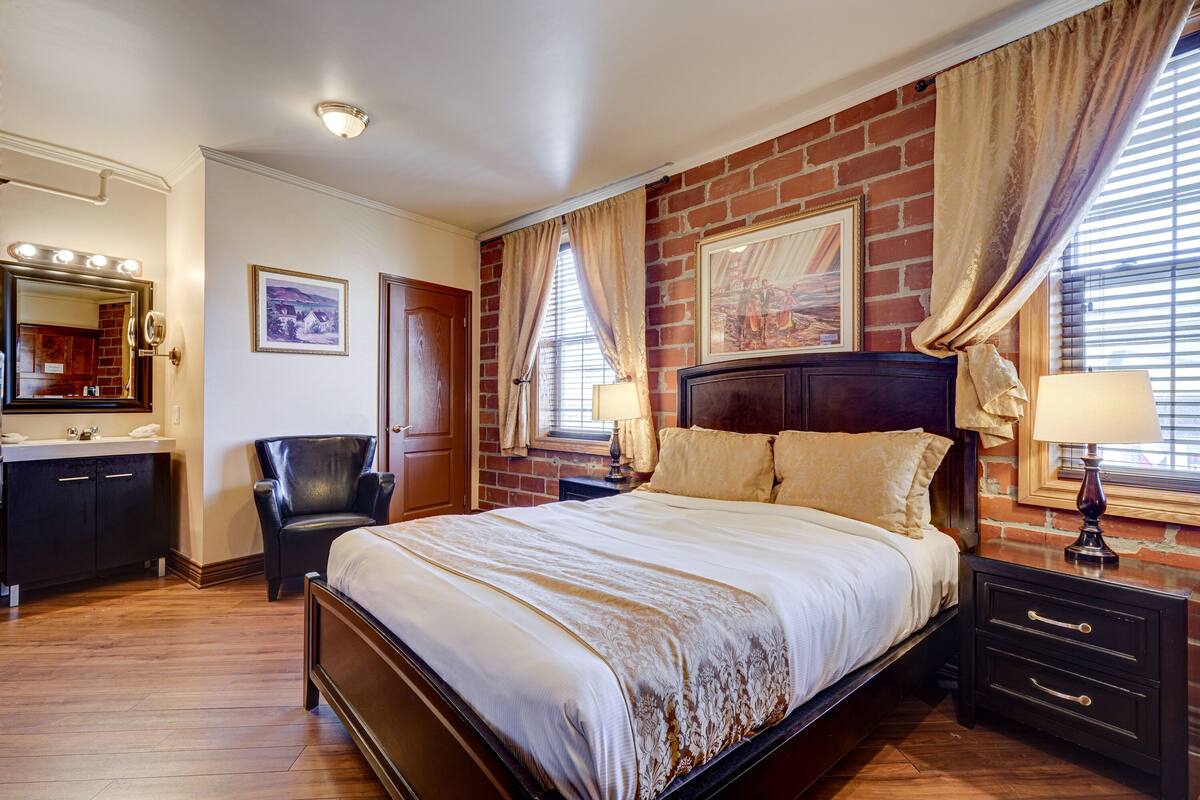 Une chambre avec un mur en briques, un grand lit, une coiffeuse avec un miroir et une chaise.