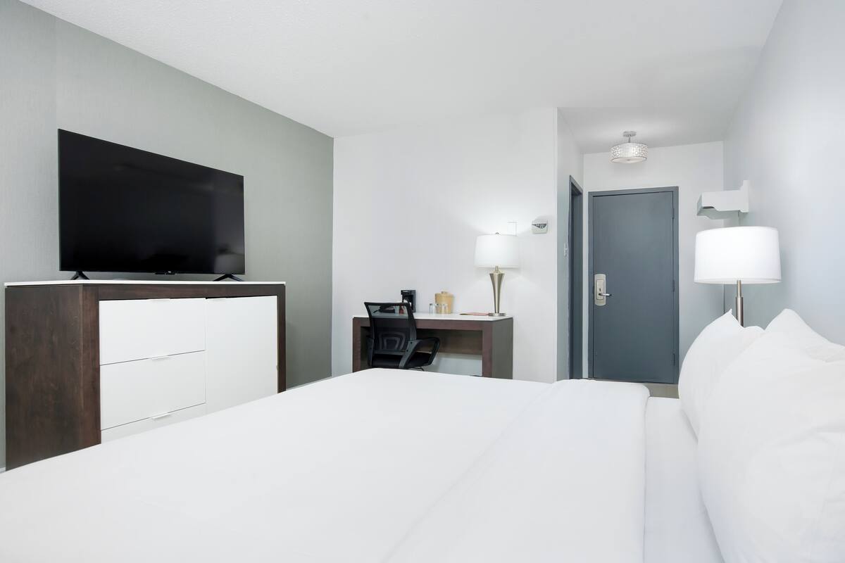 Une chambre d’hôtel avec un lit, un bureau, une chaise, une télévision et une porte.
