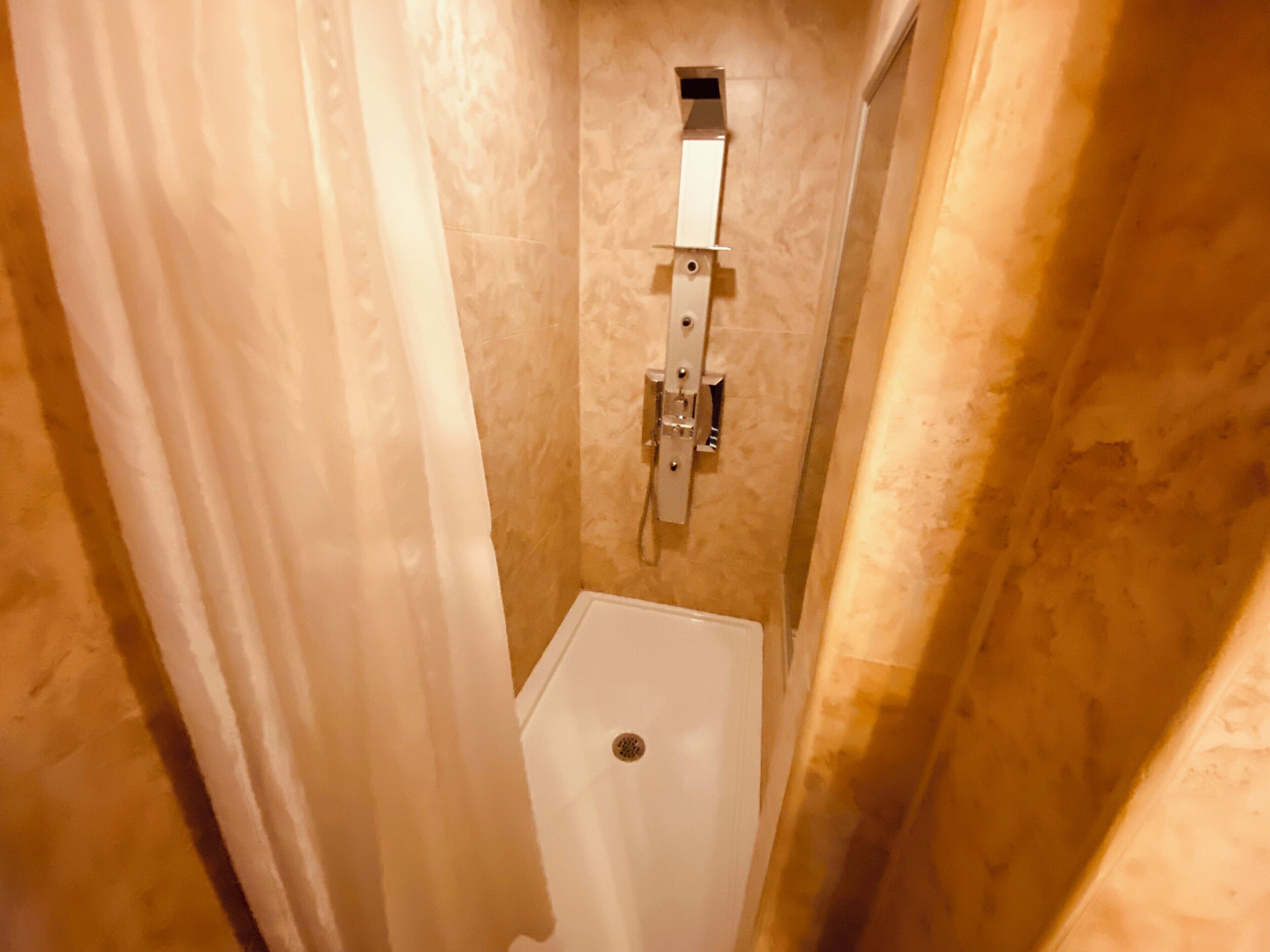 A narrow bathroom with a white toilet, a towel rack, and a shower control panel.