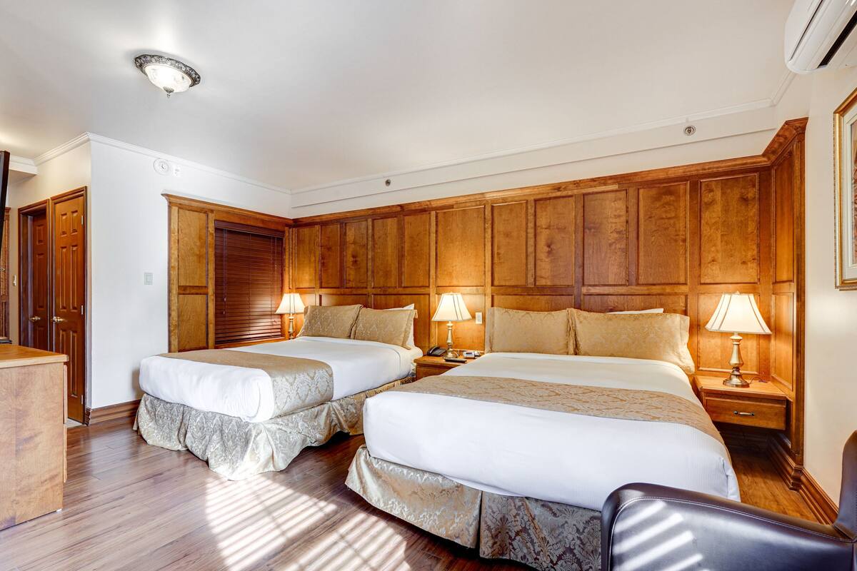 Une chambre d’hôtel avec deux lits, des boiseries, un bureau et une chaise.