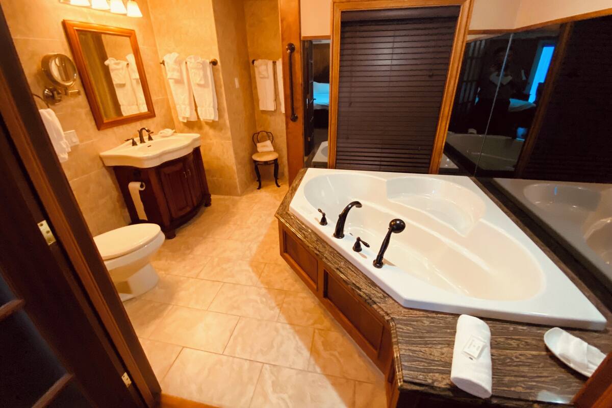 Une salle de bain moderne avec une grande baignoire, un lavabo et des toilettes. On y trouve plusieurs serviettes et une chaise.