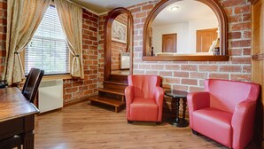 A room with brick walls, a wooden floor, a red leather chair, a wooden table, and a large mirror. - Le Grand Hôtel (Baie Comeau)