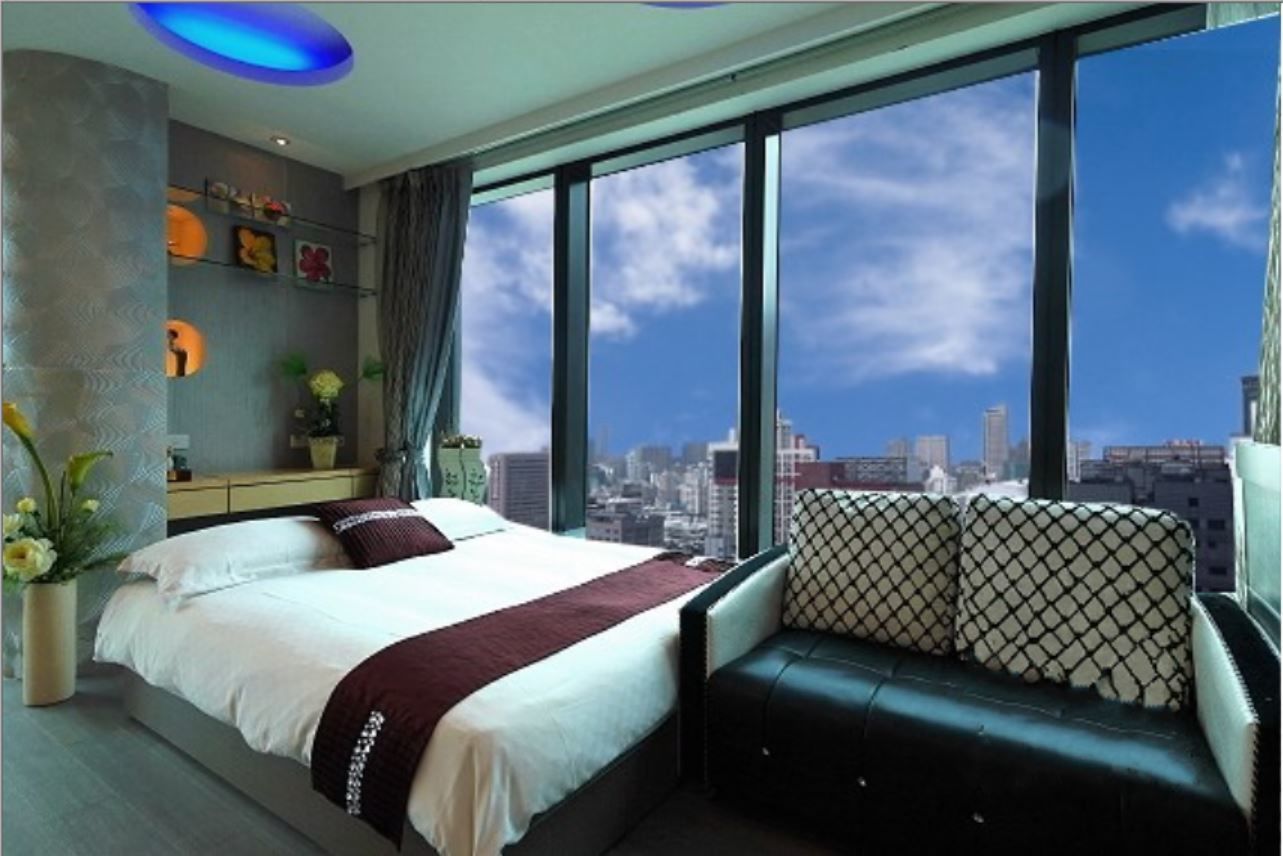 A modern hotel room with a large bed, a seating area with patterned cushions, a city view, and decorative wall art.