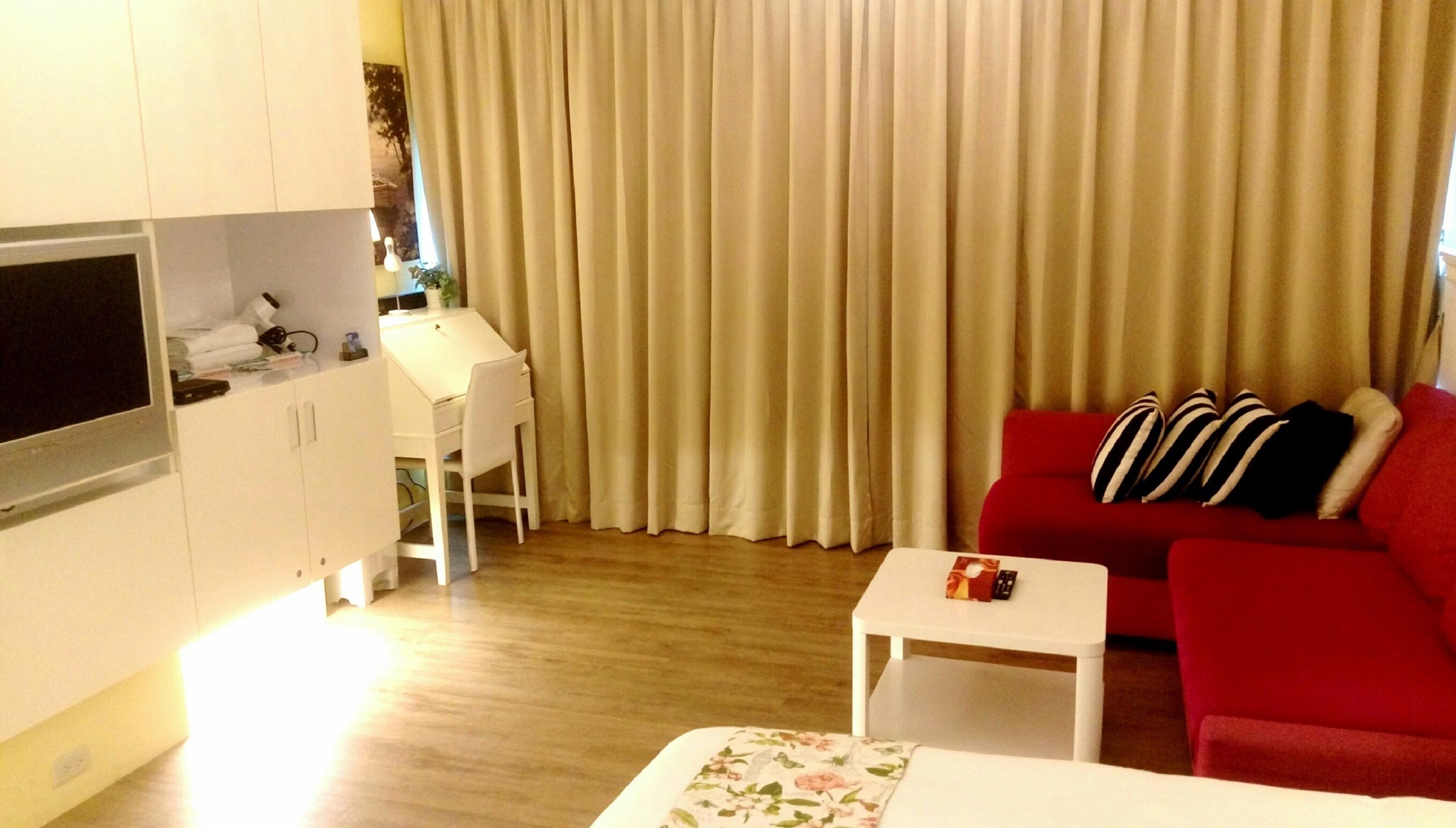 Ein gemütlicher Wohnraum mit Fernseher, Esstisch, rotem Sofa und weißem Sessel.