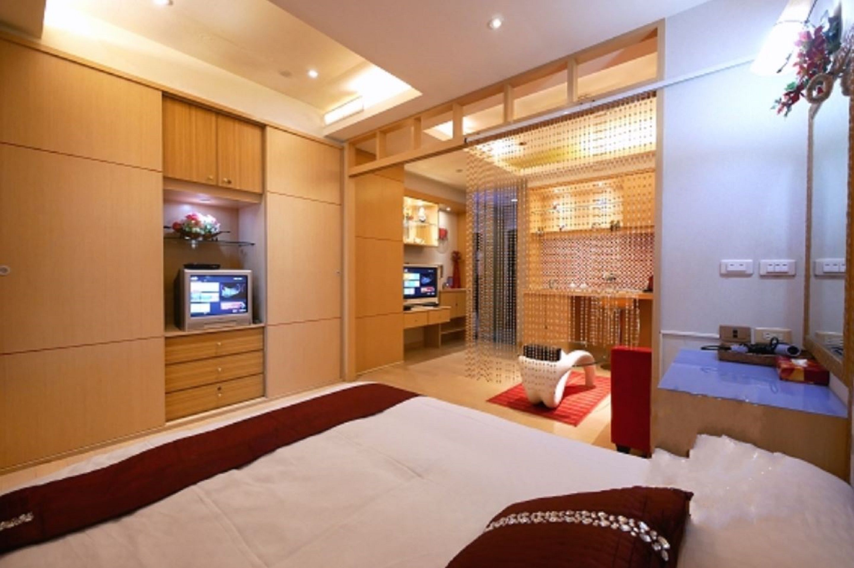 Una habitación de hotel moderna con una cama grande, un televisor, un escritorio con una computadora y una zona de estar con una silla y una mesita.