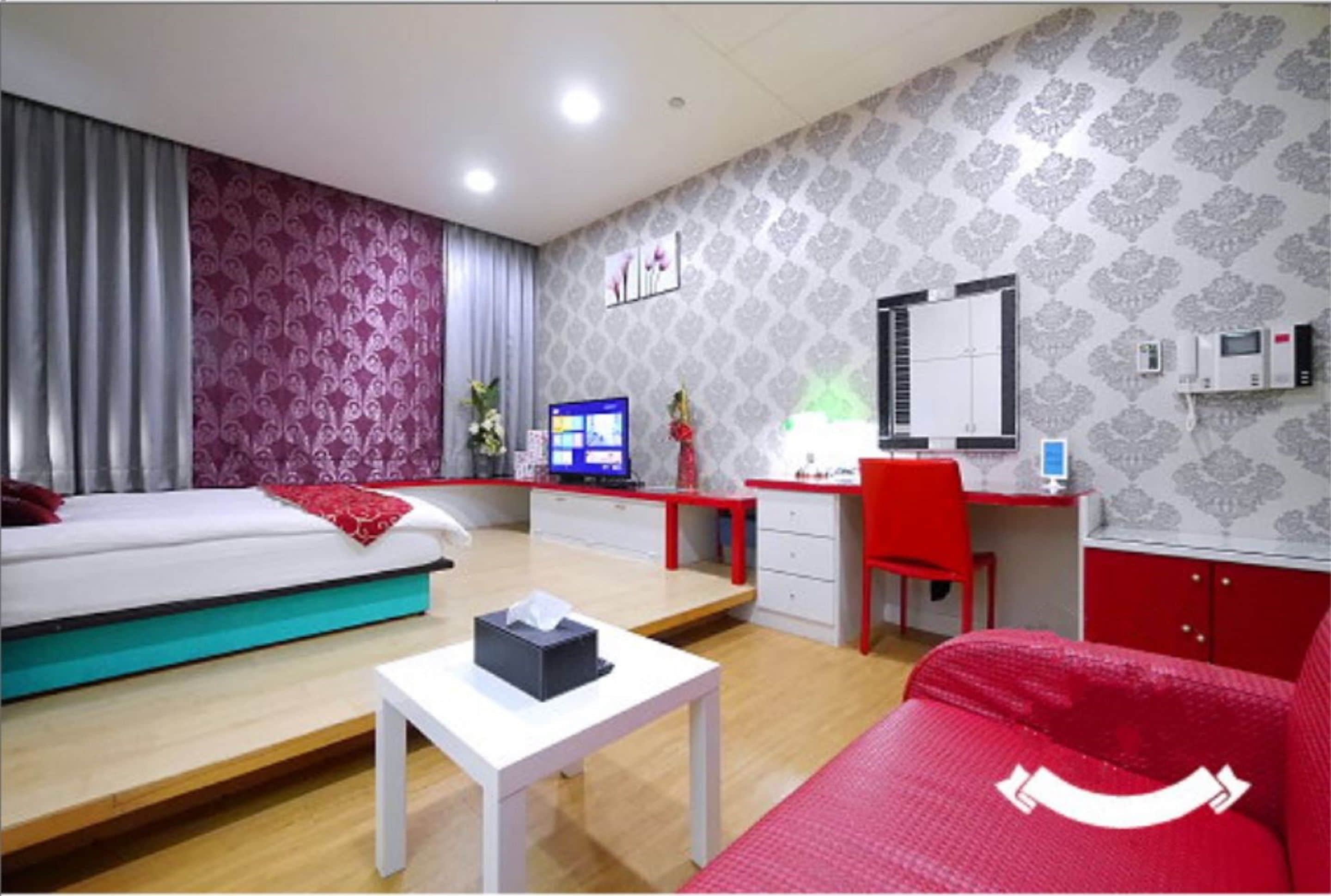 A hotel room with a bed, a desk, a chair, a small table, a mirror, and a window with curtains.