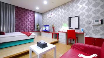 A hotel room with a bed, a desk, a chair, a small table, a mirror, and a window with curtains.