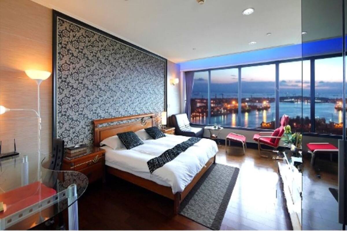 A modern hotel room with a large bed, a seating area with a view of the city, and a large window.