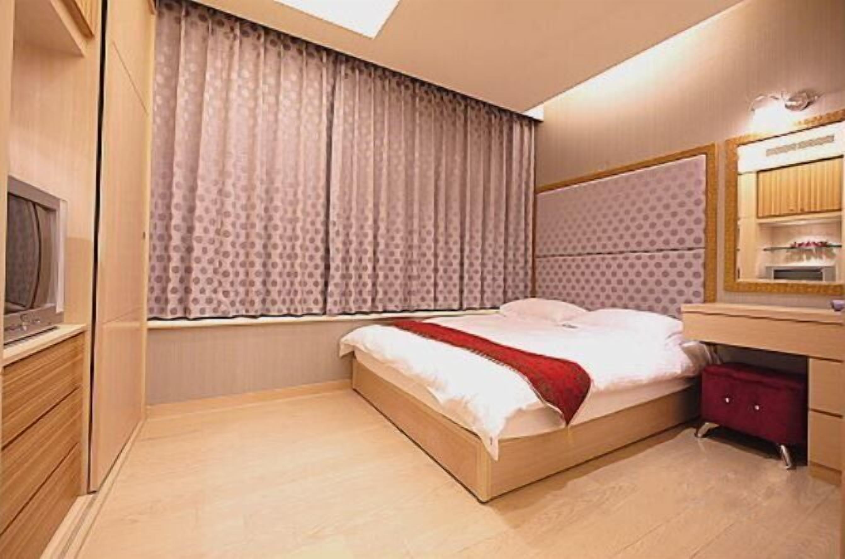 A bedroom with a bed, a window with curtains, a bedside table, a mirror, and a wardrobe.