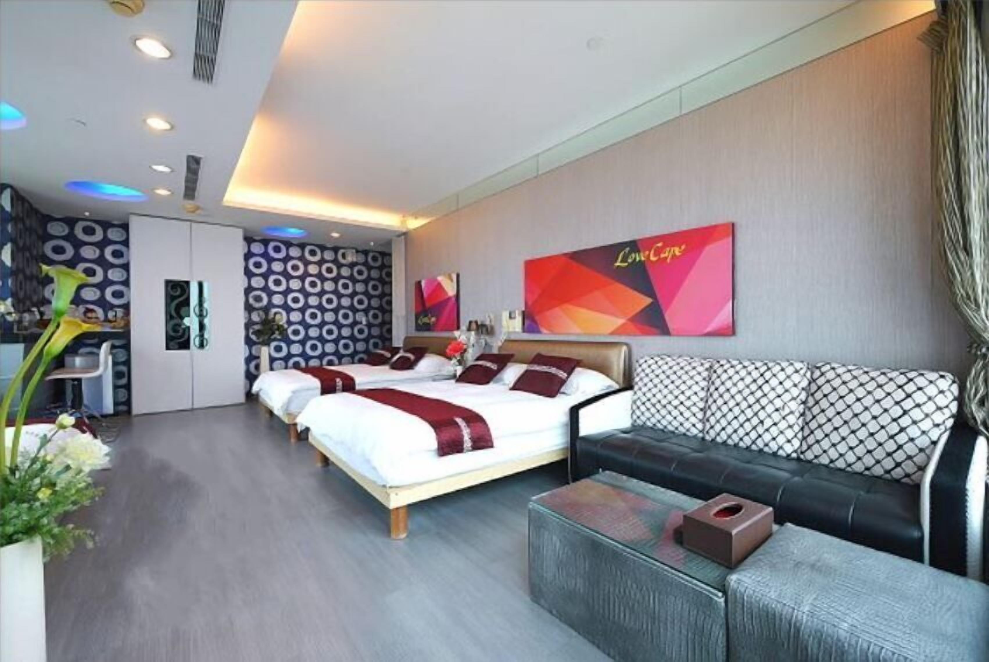 Quarto de hotel moderno com cama, sofá, mesinha e um objeto decorativo na parede.
