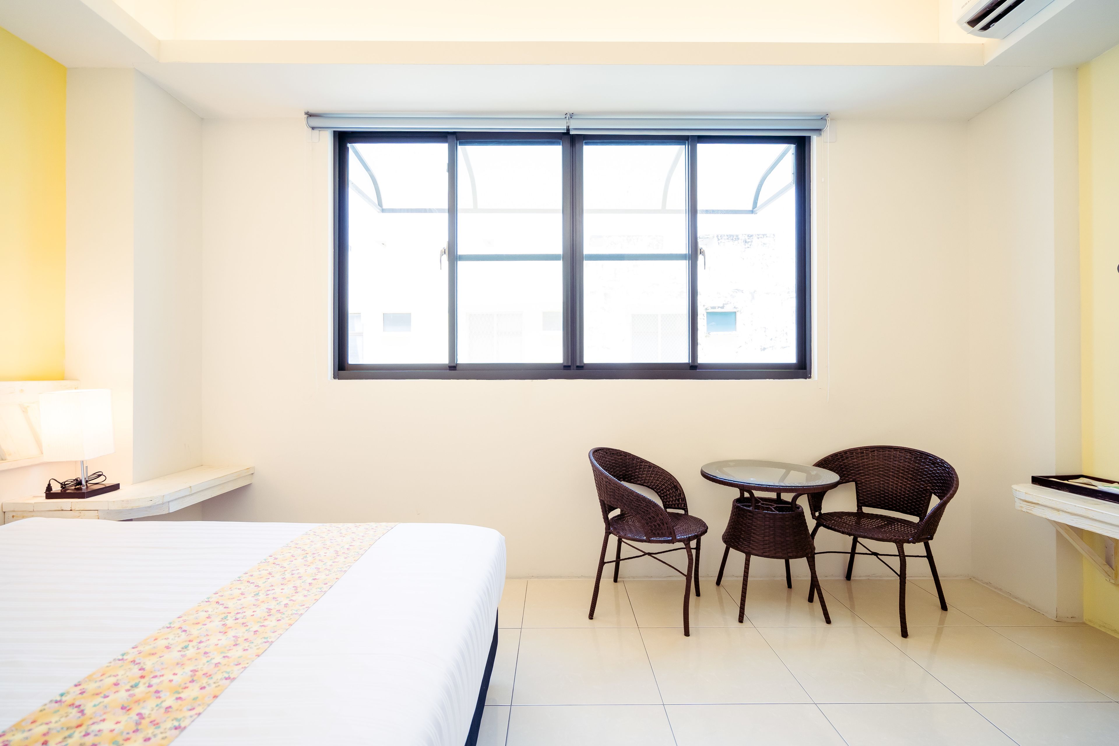A hotel room with a bed, a small table with two chairs, a window, and a desk with a chair.