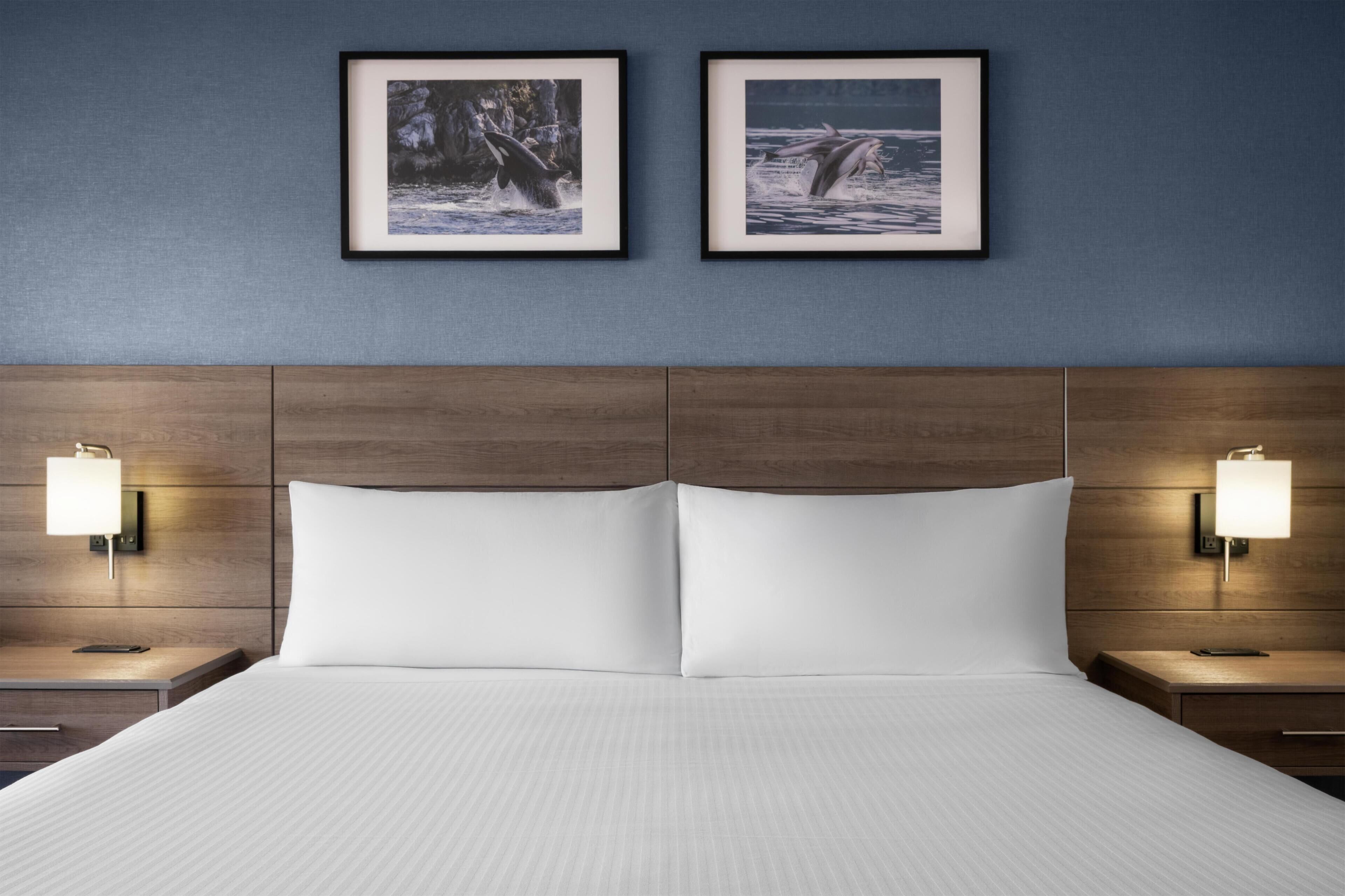 A hotel room with a large bed, two framed pictures on the wall, and bedside lamps.