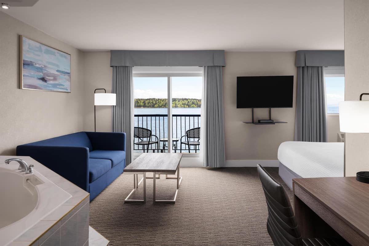 A hotel room with a balcony, a sofa, a bed, a TV, and a desk.
