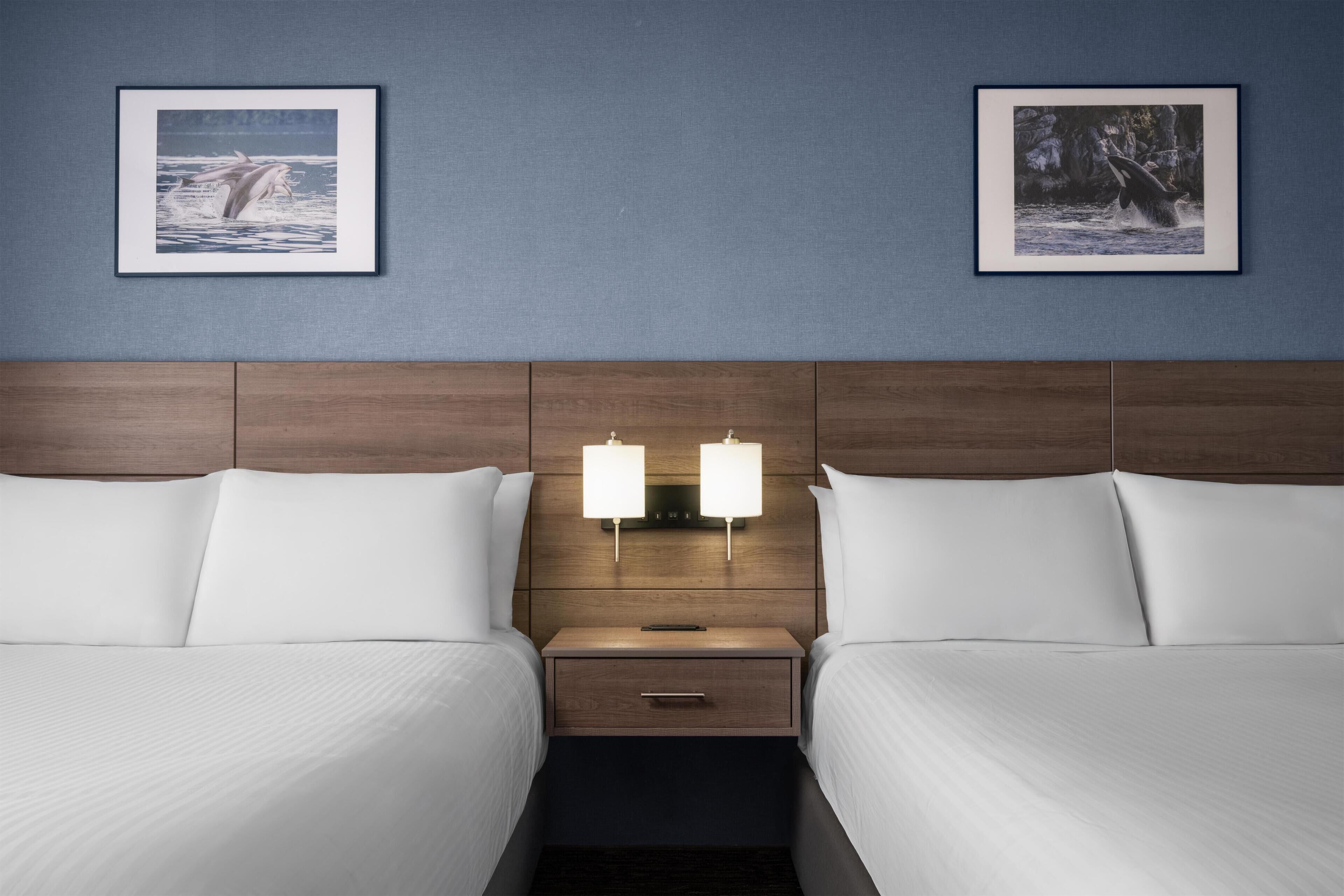 Ein Hotelzimmer mit zwei Betten, einem Holzkopfteil, Nachttischlampen und gerahmten Bildern an der Wand.