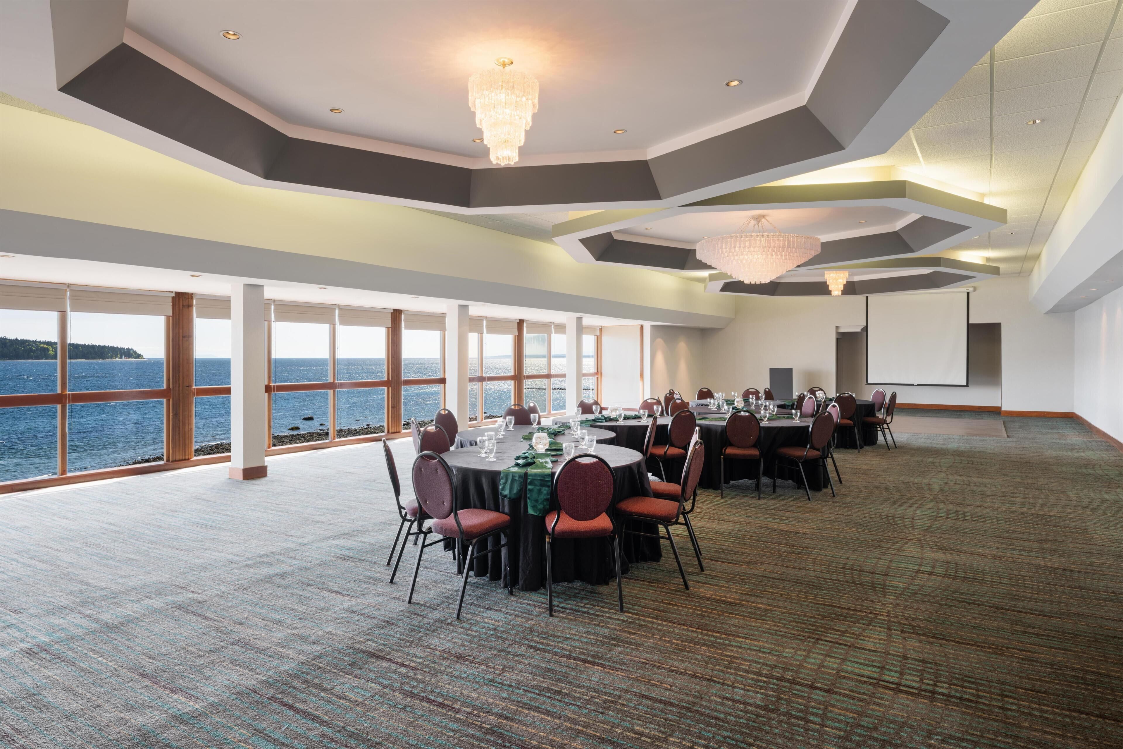 A conference room with a panoramic sea view, large windows, and a modern chandelier.