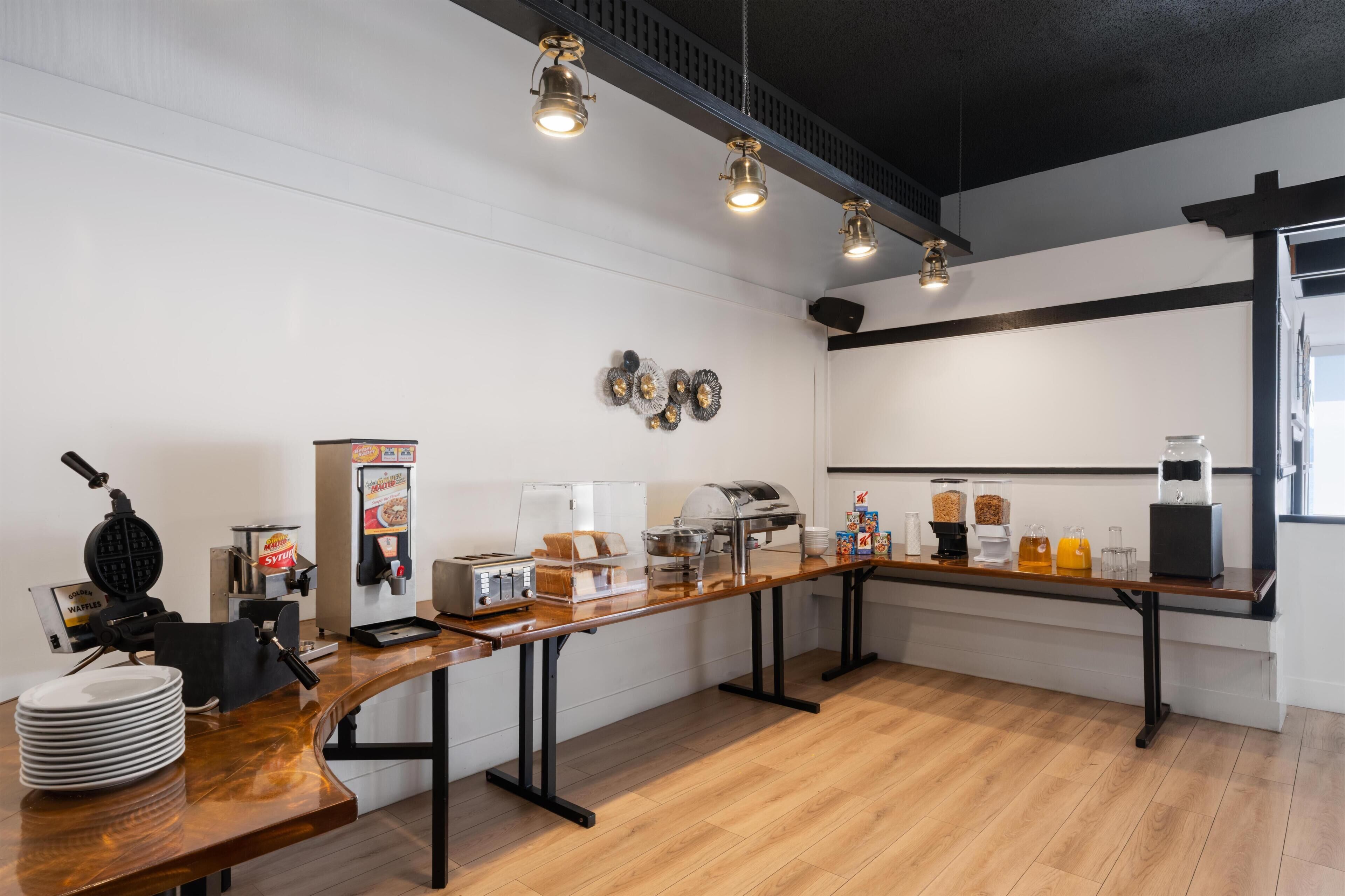 Een ontbijtbuffet met een wafelijzer, koffieapparaat en sapsdispensers.