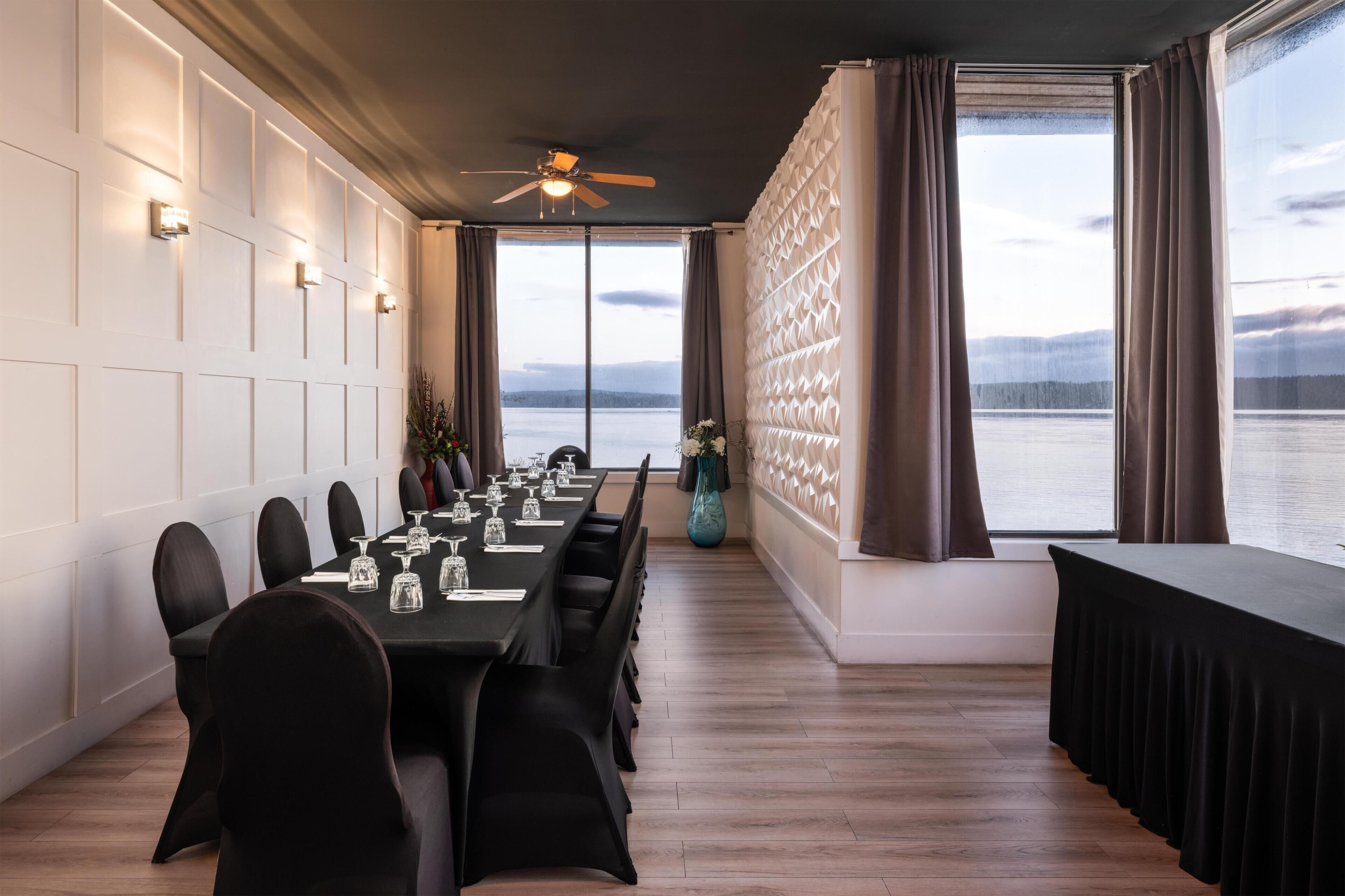 A conference room with a long table, chairs, a ceiling fan, and a view of a body of water.