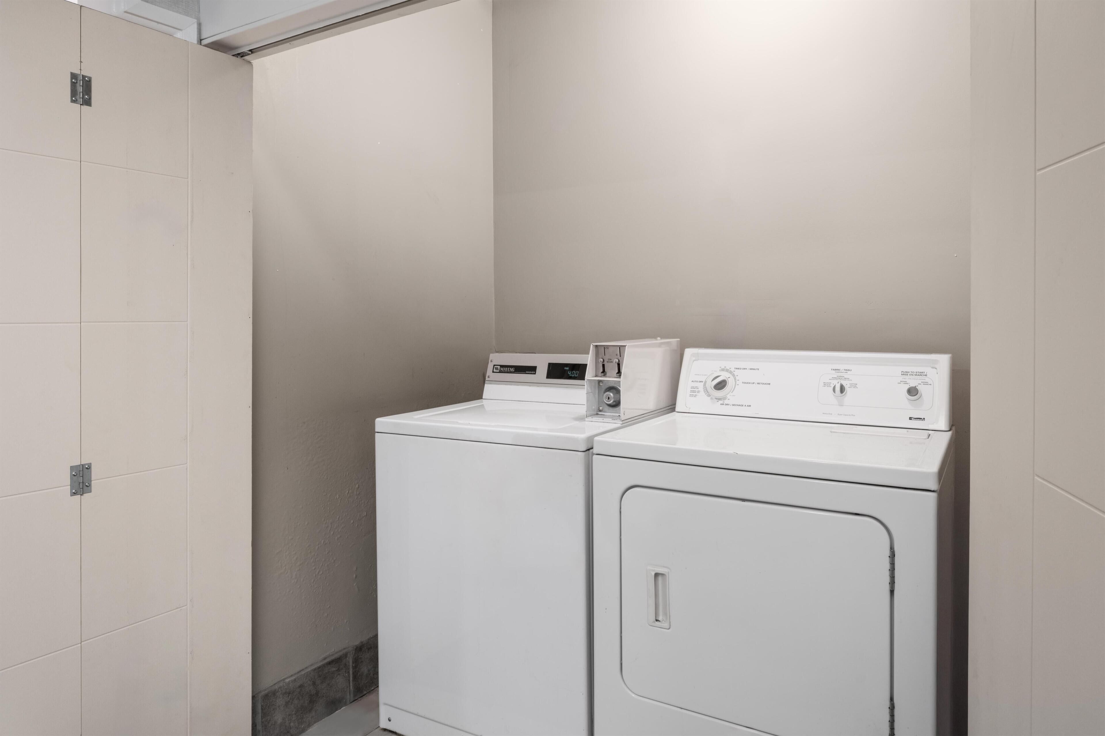 A laundry room with two stacked washers and dryers, a tiled floor, and a plain wall.