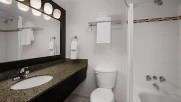 Baño con lavamanos de encimera de granito, inodoro blanco, ducha con puerta de vidrio y espejo con iluminación.