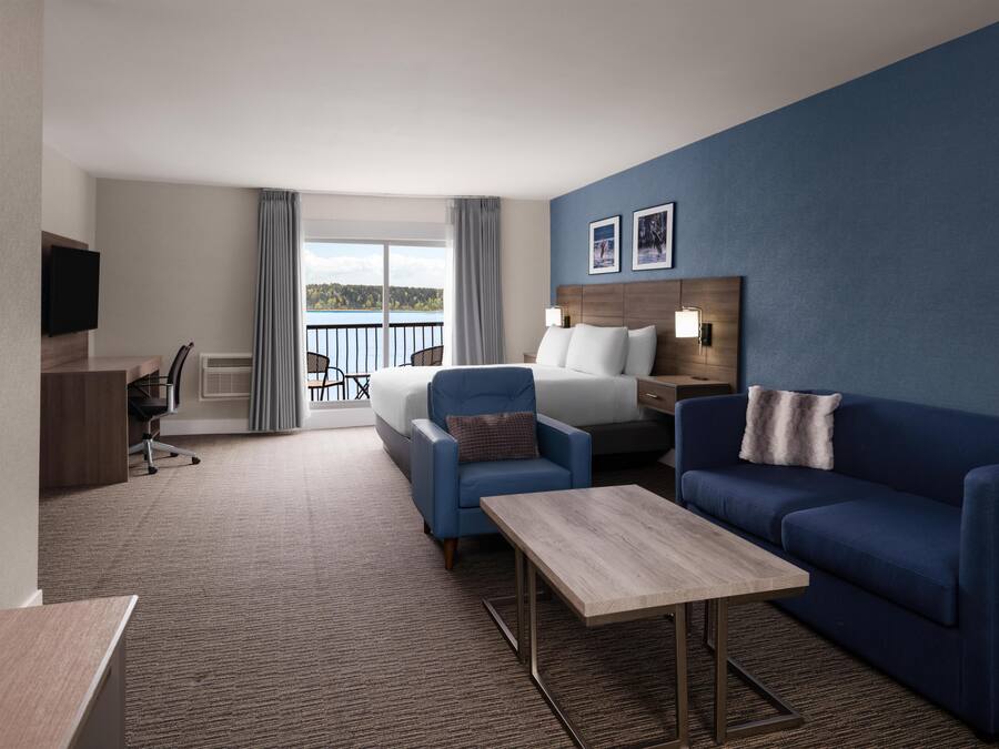 Une chambre d’hôtel avec un lit, un canapé bleu, une petite table, une télévision, un bureau et un balcon avec vue.