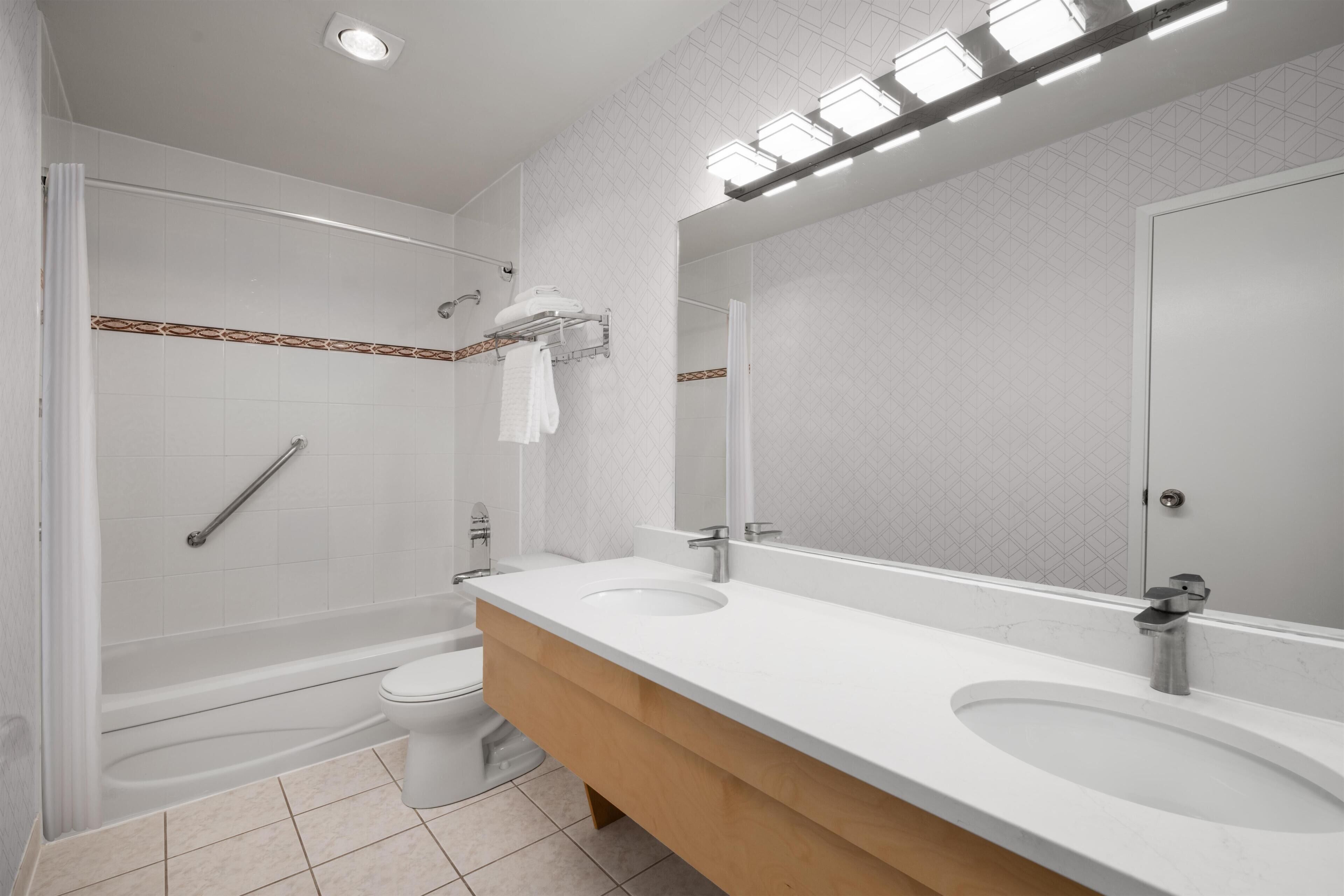 A modern bathroom with a bathtub, toilet, and two sinks.