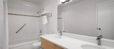 A modern bathroom with a bathtub, toilet, and two sinks.