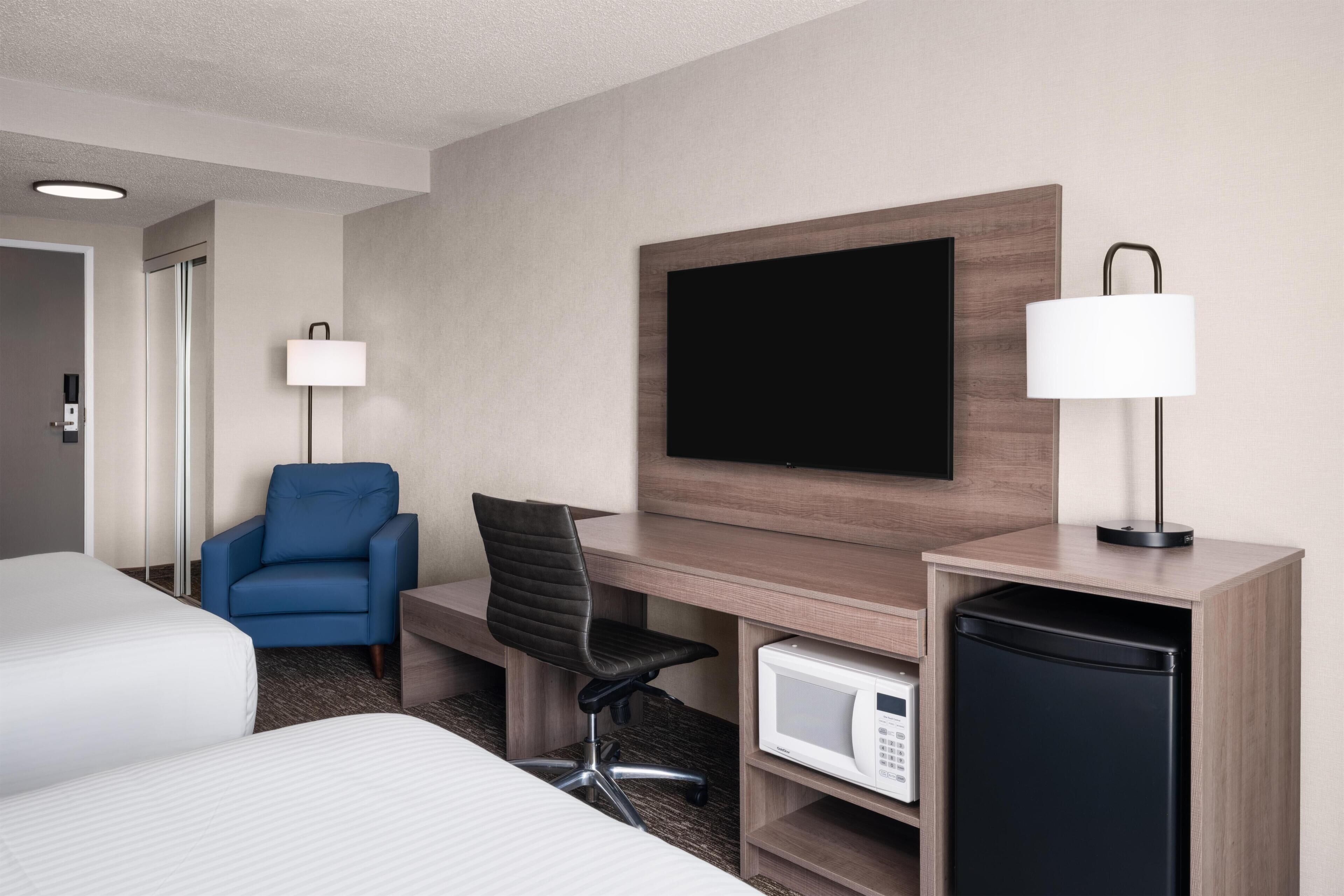 Ein Hotelzimmer mit Bett, Schreibtisch mit Stuhl, Fernseher, Lampe und einer Mikrowelle.