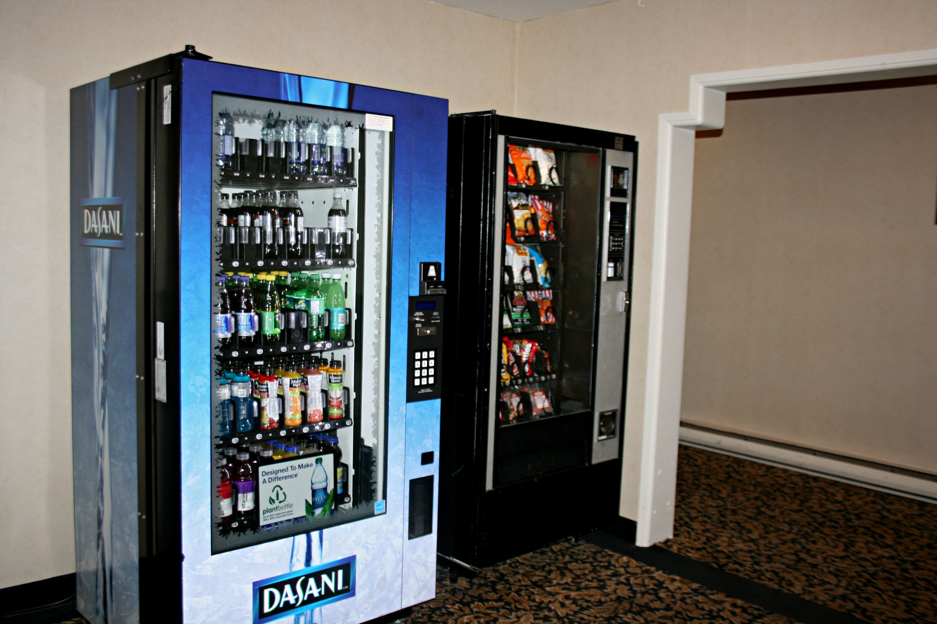 Two Dasani water vending machines in a hallway with a patterned carpet.